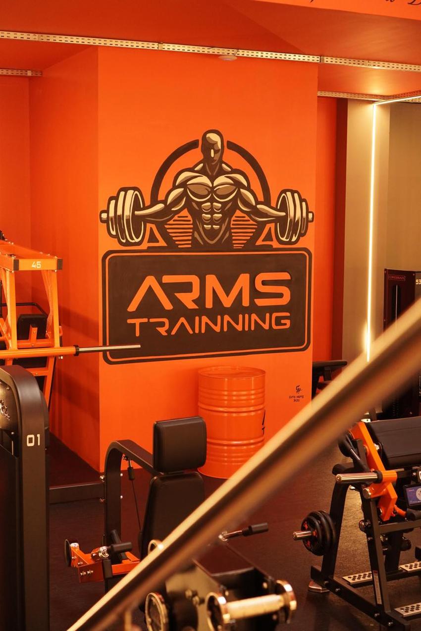 Mural do logotipo Arms Trainning pintado em preto sobre a parede laranja do salão