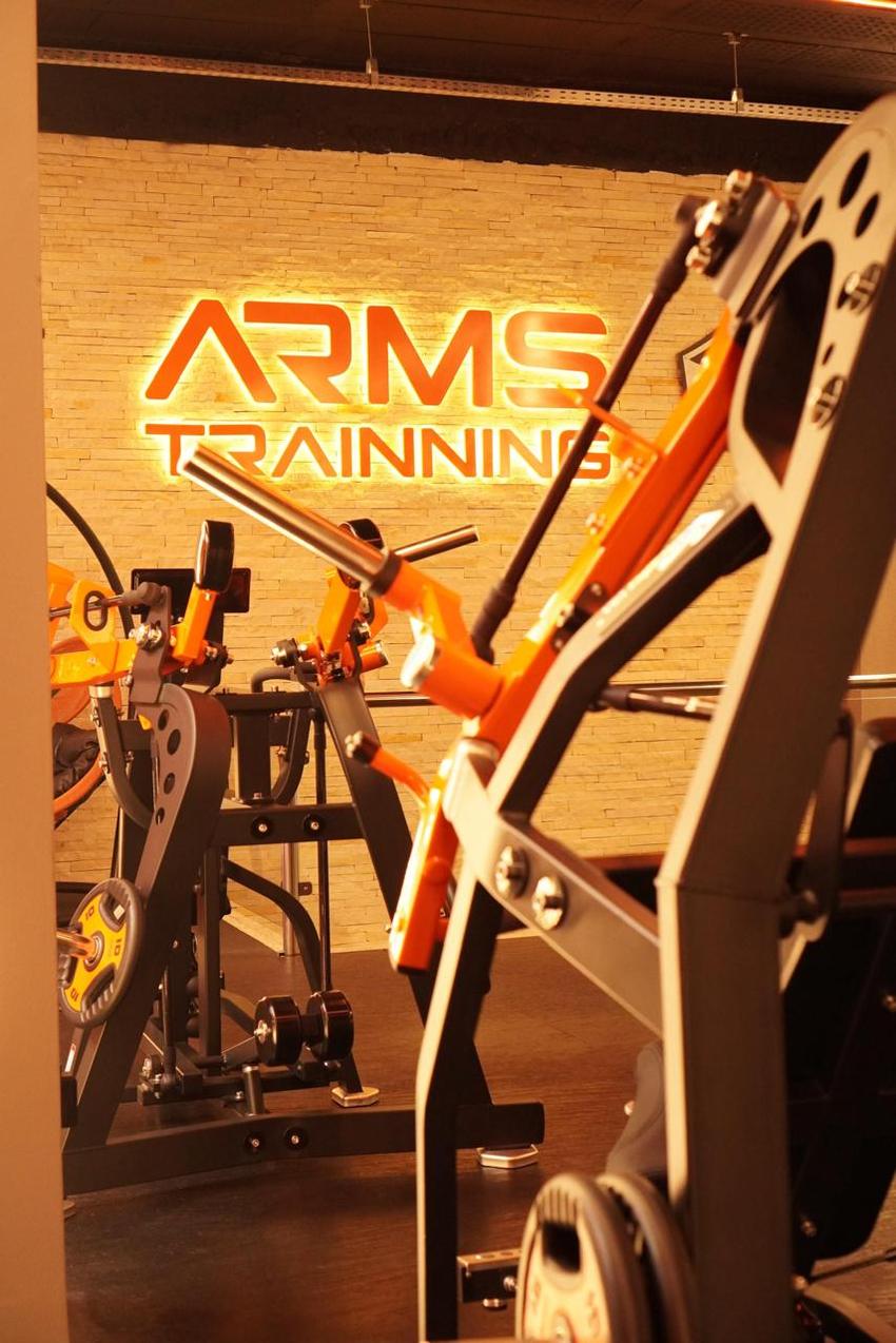 Máquinas articuladas laranja diante do letreiro iluminado Arms Trainning na parede de pedra