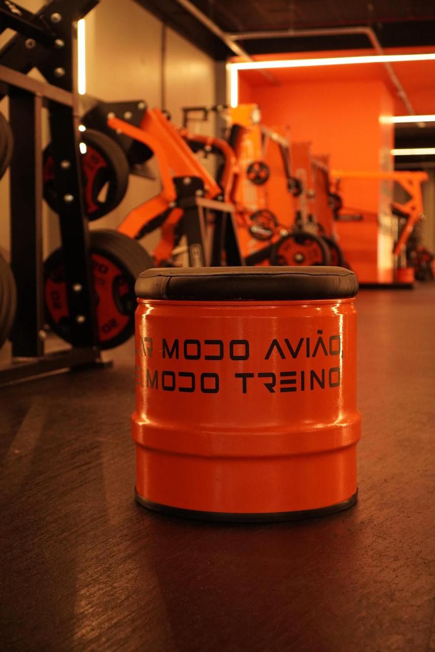 Banquinho laranja em formato de tambor com a frase "modo avião, modo treino" impressa na lateral