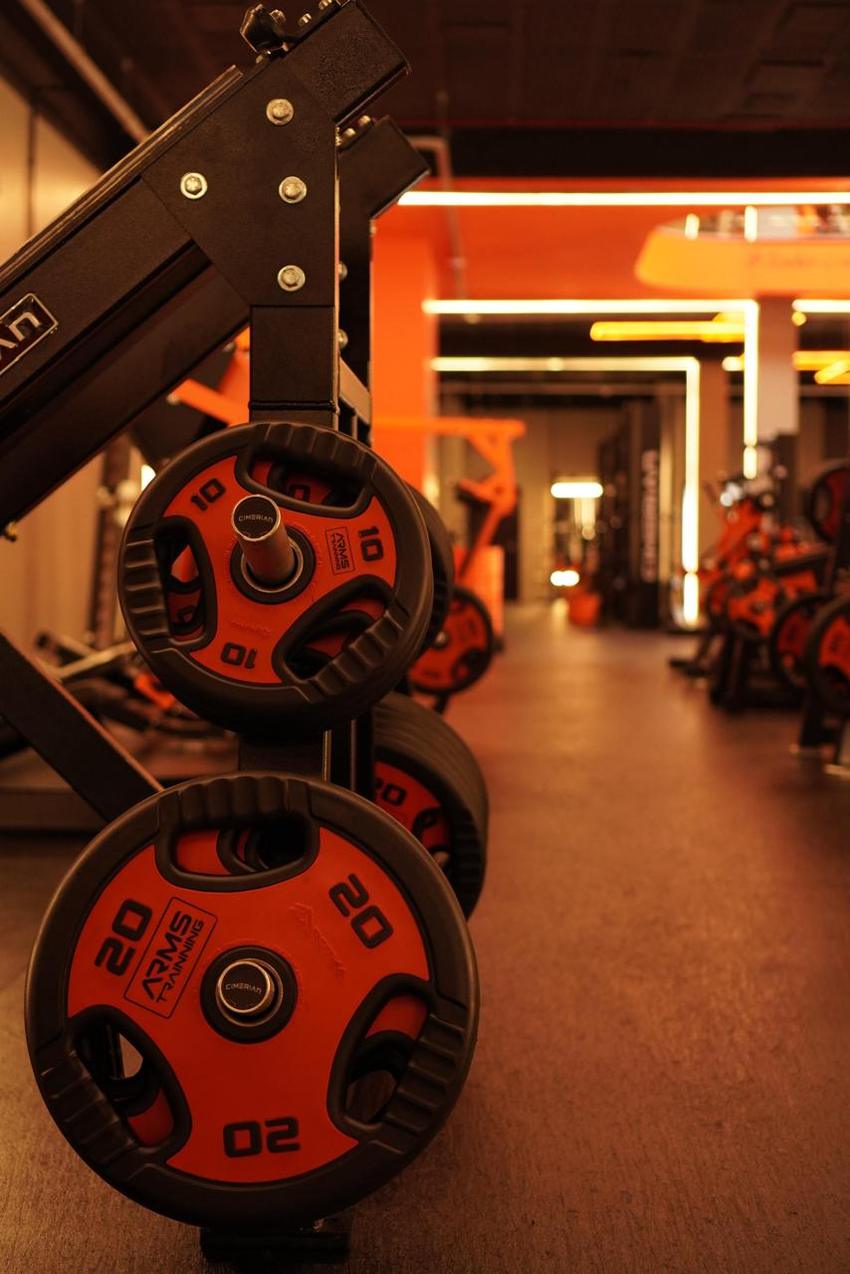 Close das anilhas de 10 e 20 kg com a marca Arms Trainning, e o corredor das bikes ao fundo
