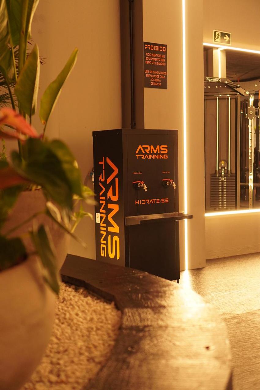 Bebedouro personalizado Arms Trainning com a inscrição "hidrate-se", ao lado de um vaso de plantas